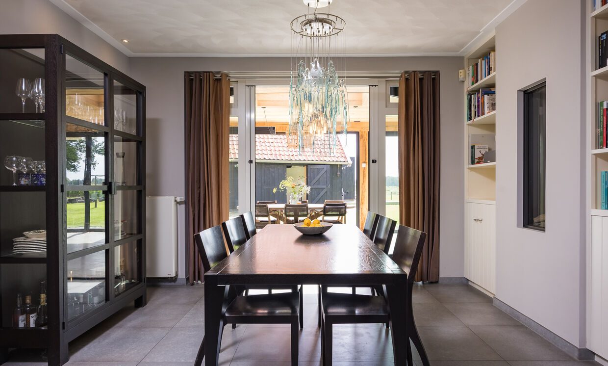 De eethoek met lange tafel en vitrinekast, met zicht naar de serre