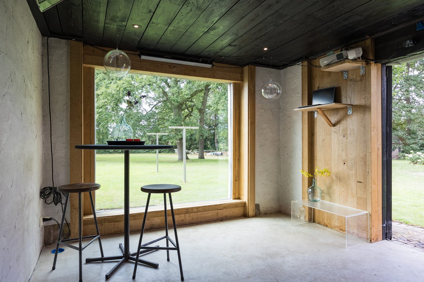 De bar met een grote glaspui en statafel, met uitzicht op het erf