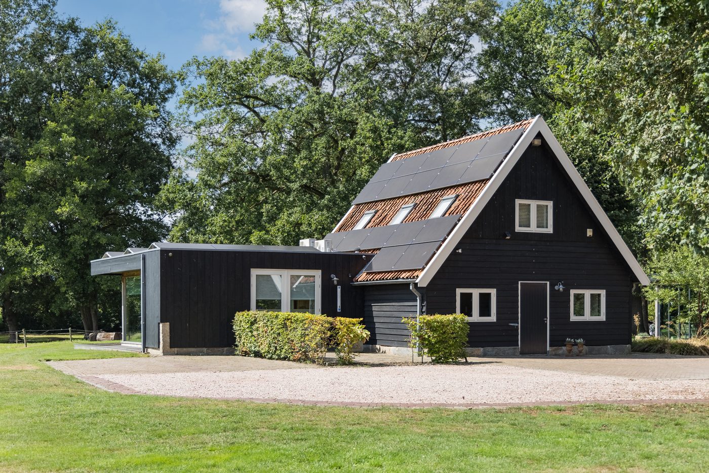 Het vrijstaande kantoorgebouw overdag, met zwarte houten gevels en het grindpad ervoor