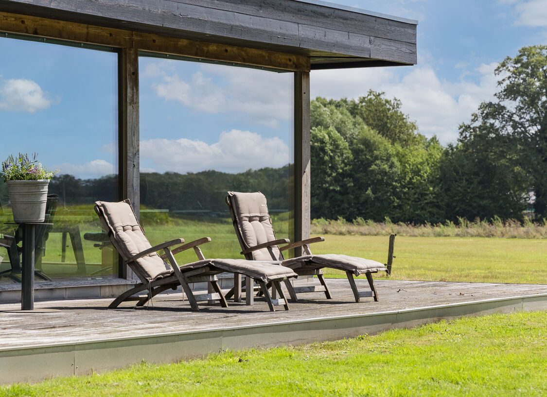 Het houten terras bij het kantoor, met ligstoelen en uitzicht over het weiland