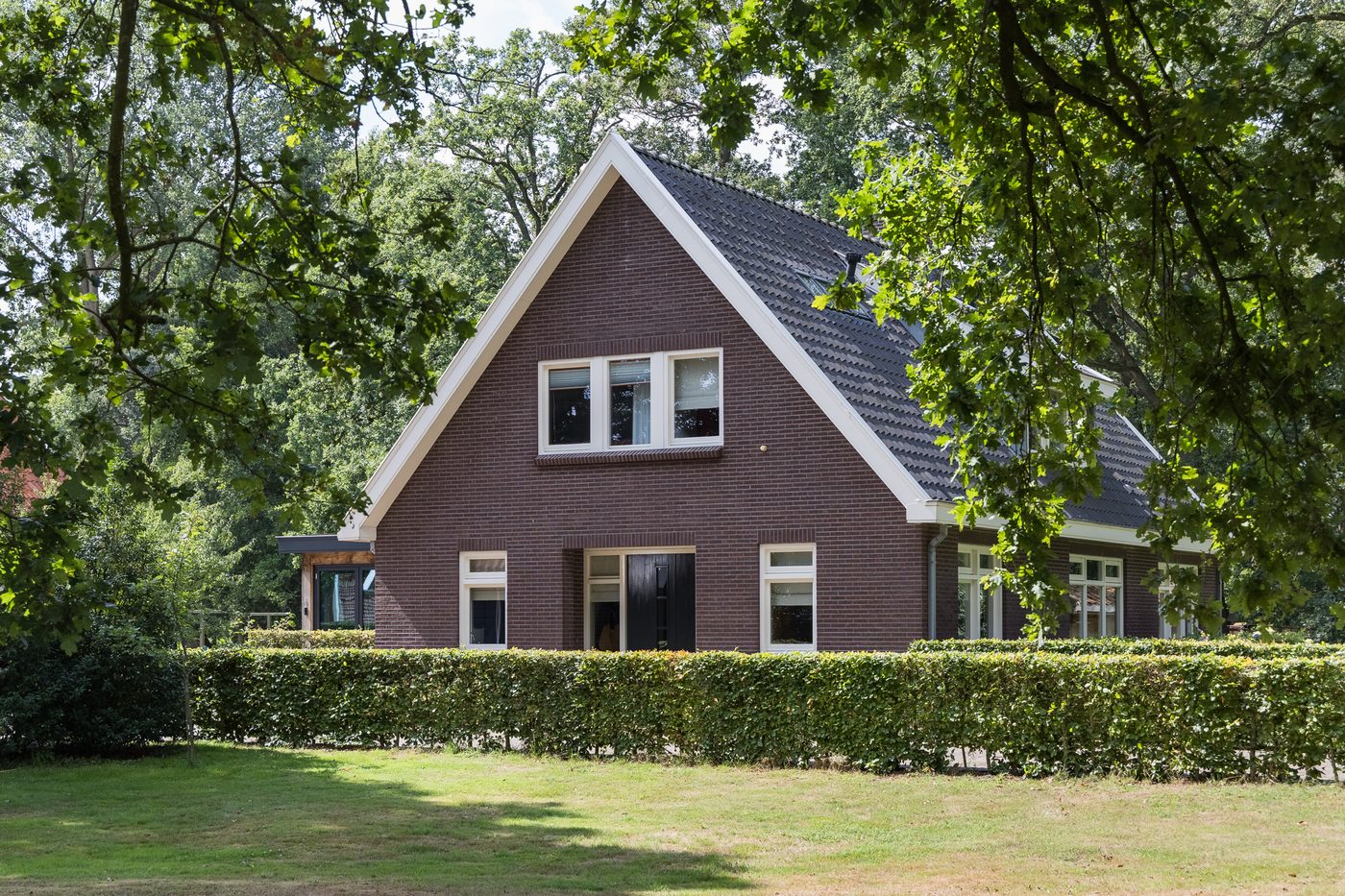 Een zijgevel van het landhuis achter de haag, tussen de bomen