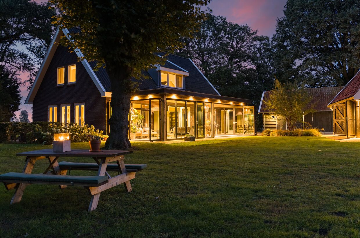 Het landhuis bij avond, met de verlichte serre achter een picknicktafel op het gazon