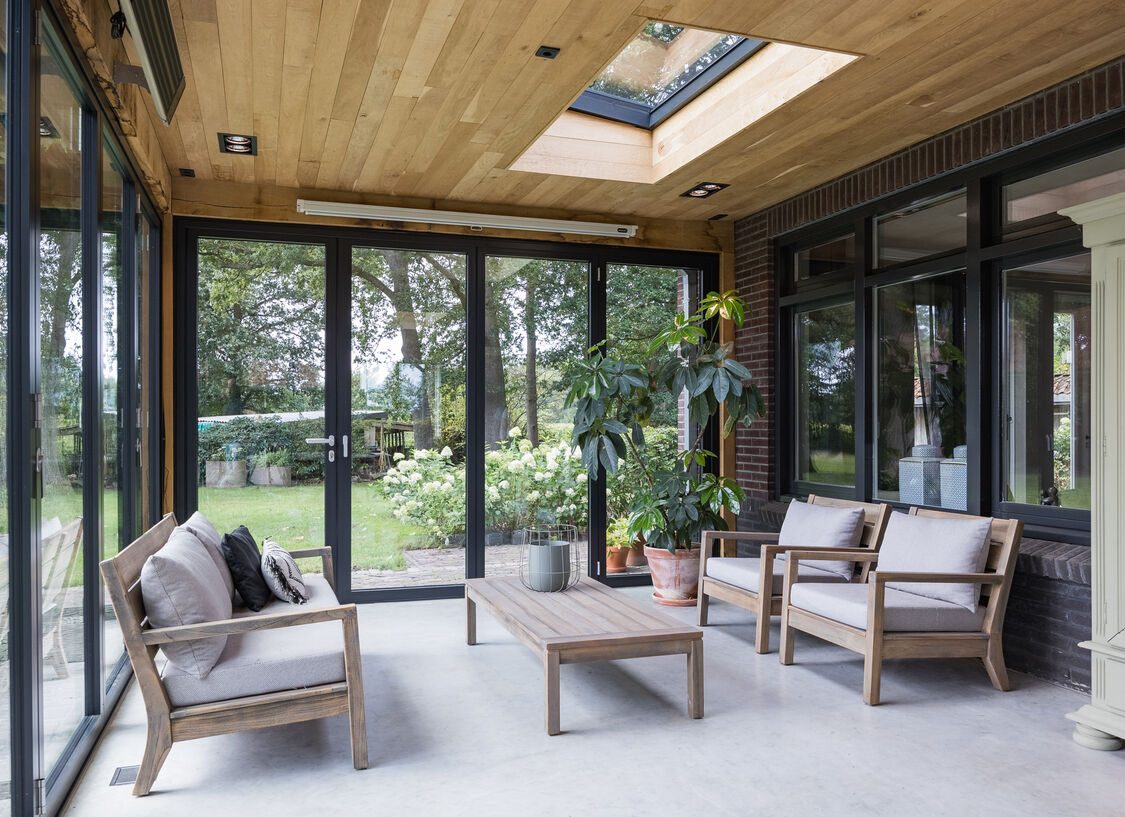 De serre met loungemeubels, houten plafond en lichtkoepel, met de harmonicadeuren naar de tuin
