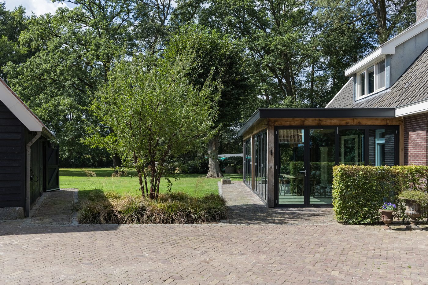 De serre aan de zijde van het klinkerplein, tussen de bomen