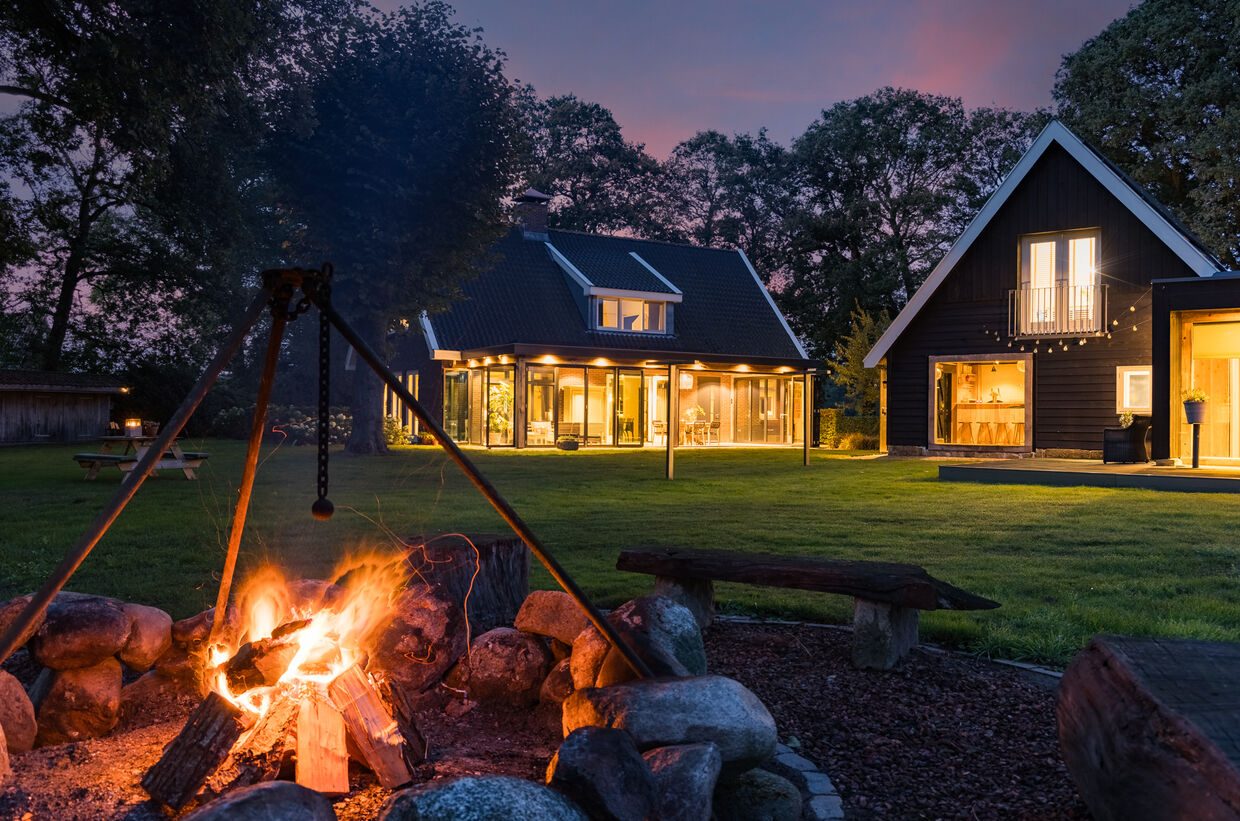 De vuurplaats bij avond, met het verlichte landhuis en kantoorgebouw op de achtergrond